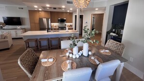 A modern kitchen with a central island, wooden dining table with woven placemats, and a chandelier. - Beautiful 3 Bedroom Poolside Oasis! (Bonita Springs)