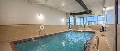 An indoor swimming pool with clear water, a lifebuoy, and a ladder.