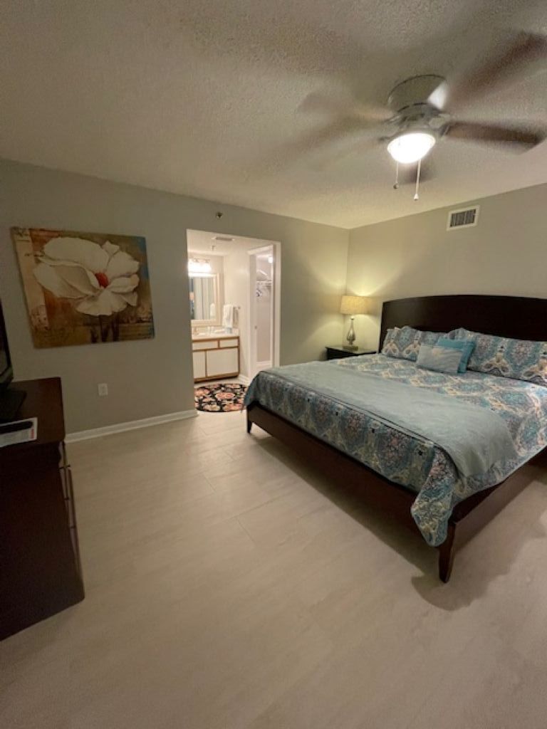 A bedroom with a bed, a ceiling fan, a nightstand, and a painting on the wall.