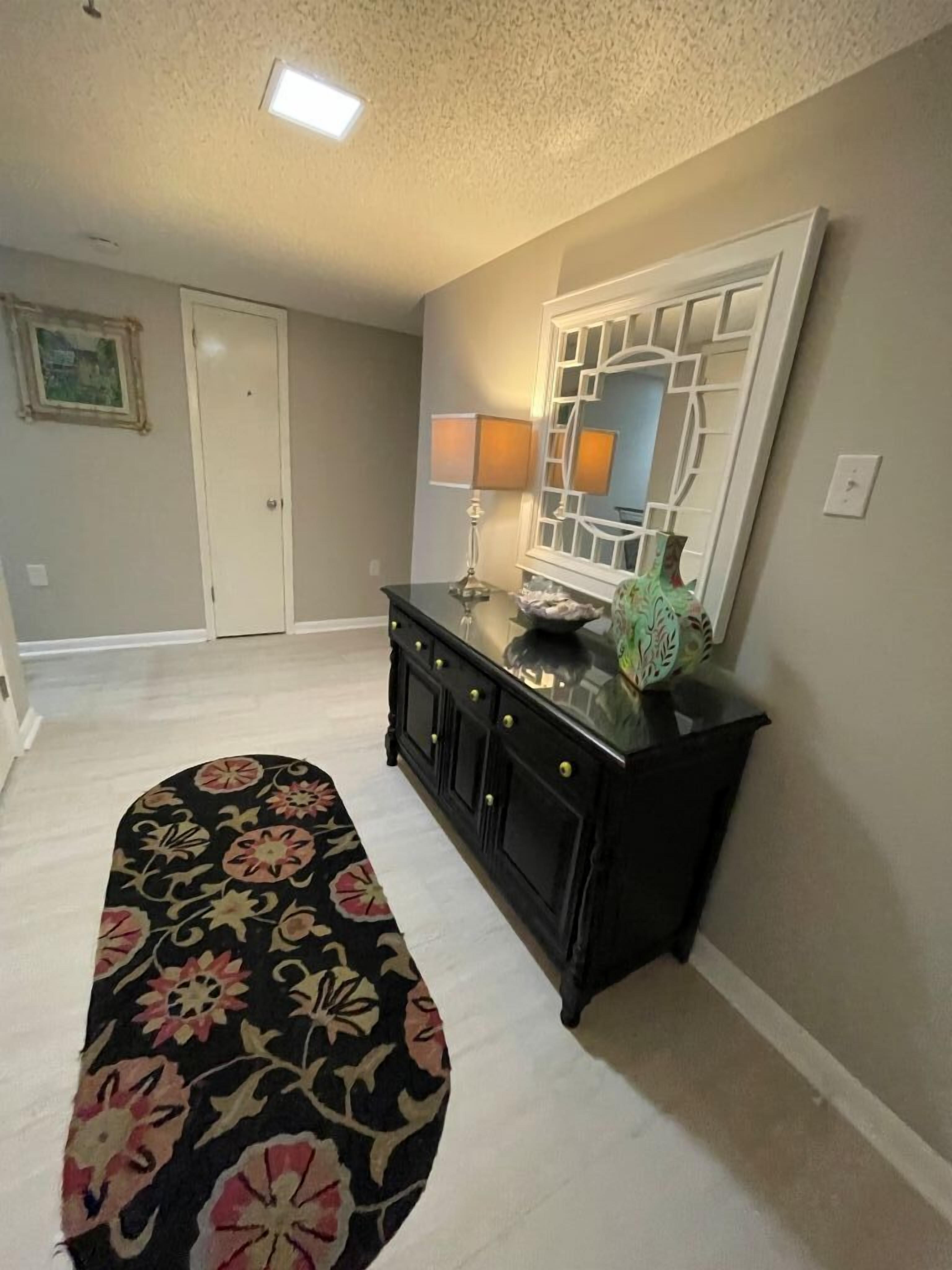 A hallway with a black console table, a mirror, and a floral rug.
