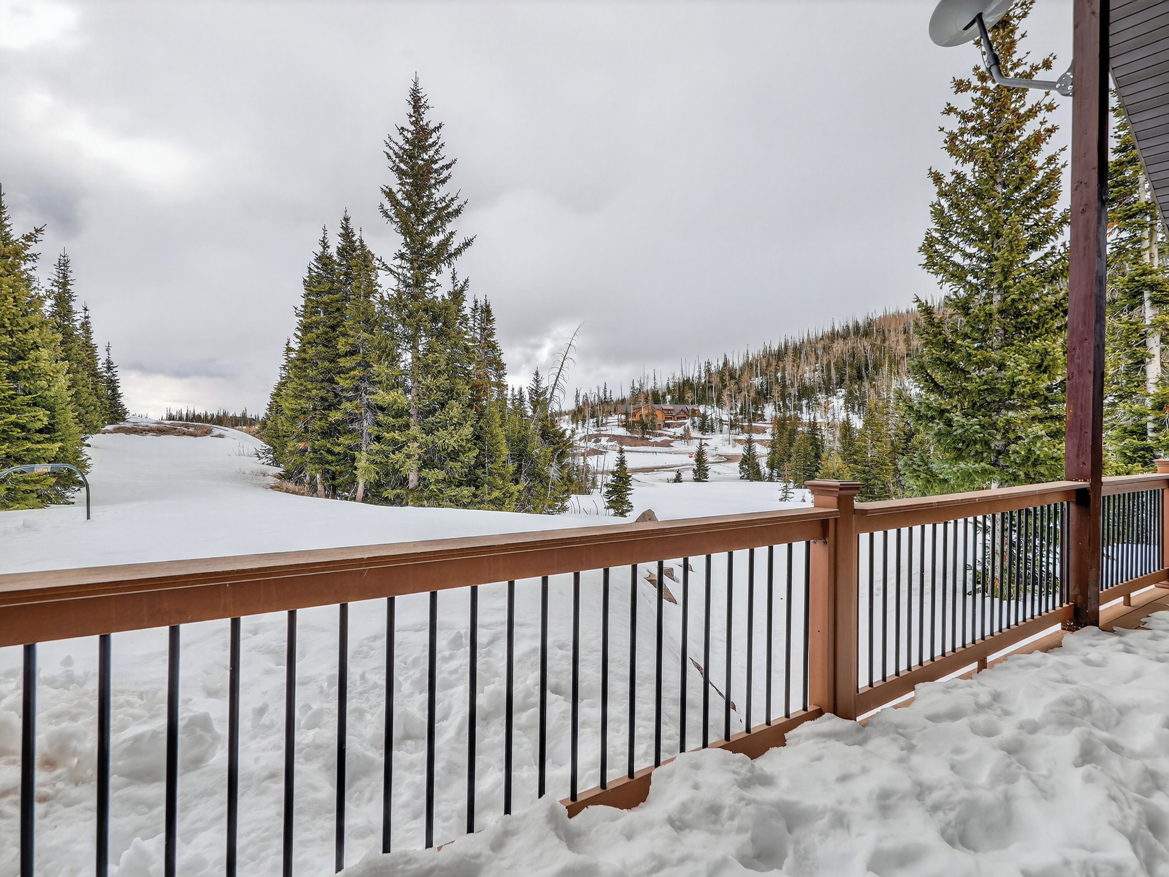 Ein mit Schnee bedeckter Balkon mit Blick auf einen Wald und ein Gebäude in der Ferne.