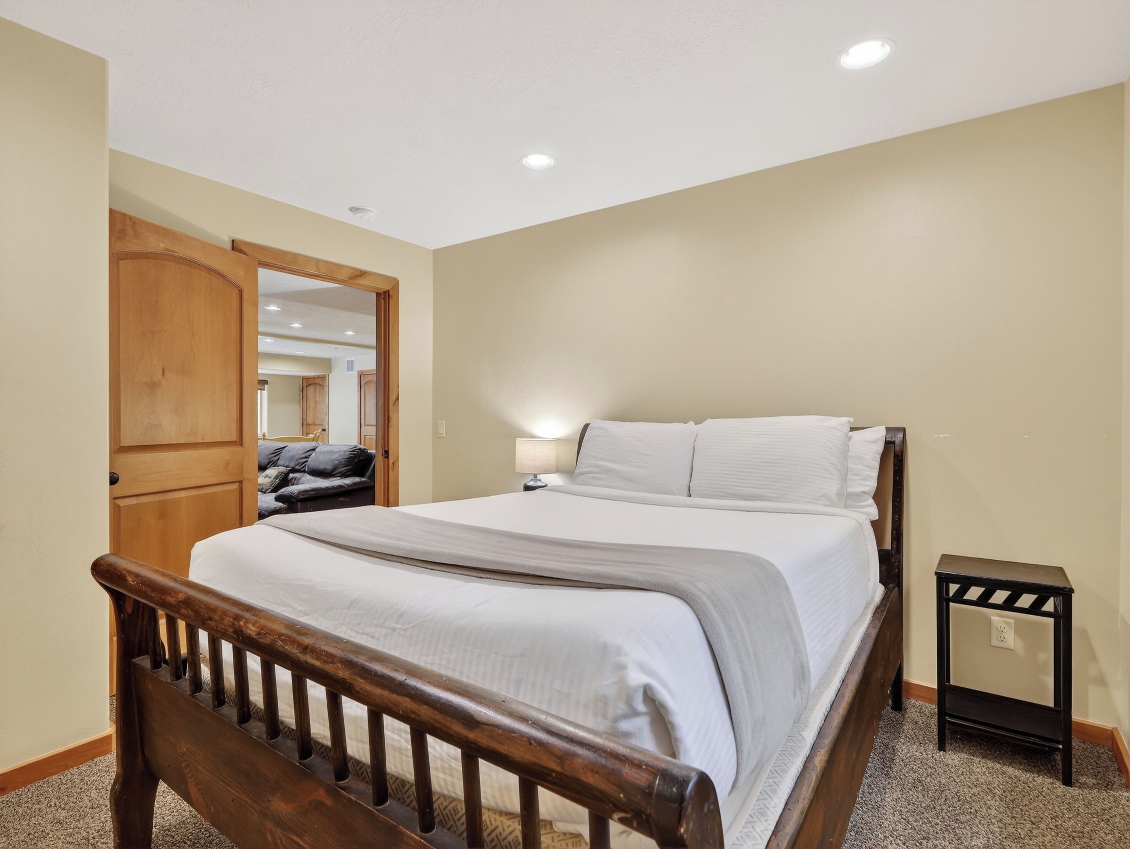 Une chambre à coucher avec un lit en bois, une table de chevet, une lampe et une porte donnant sur une autre pièce.