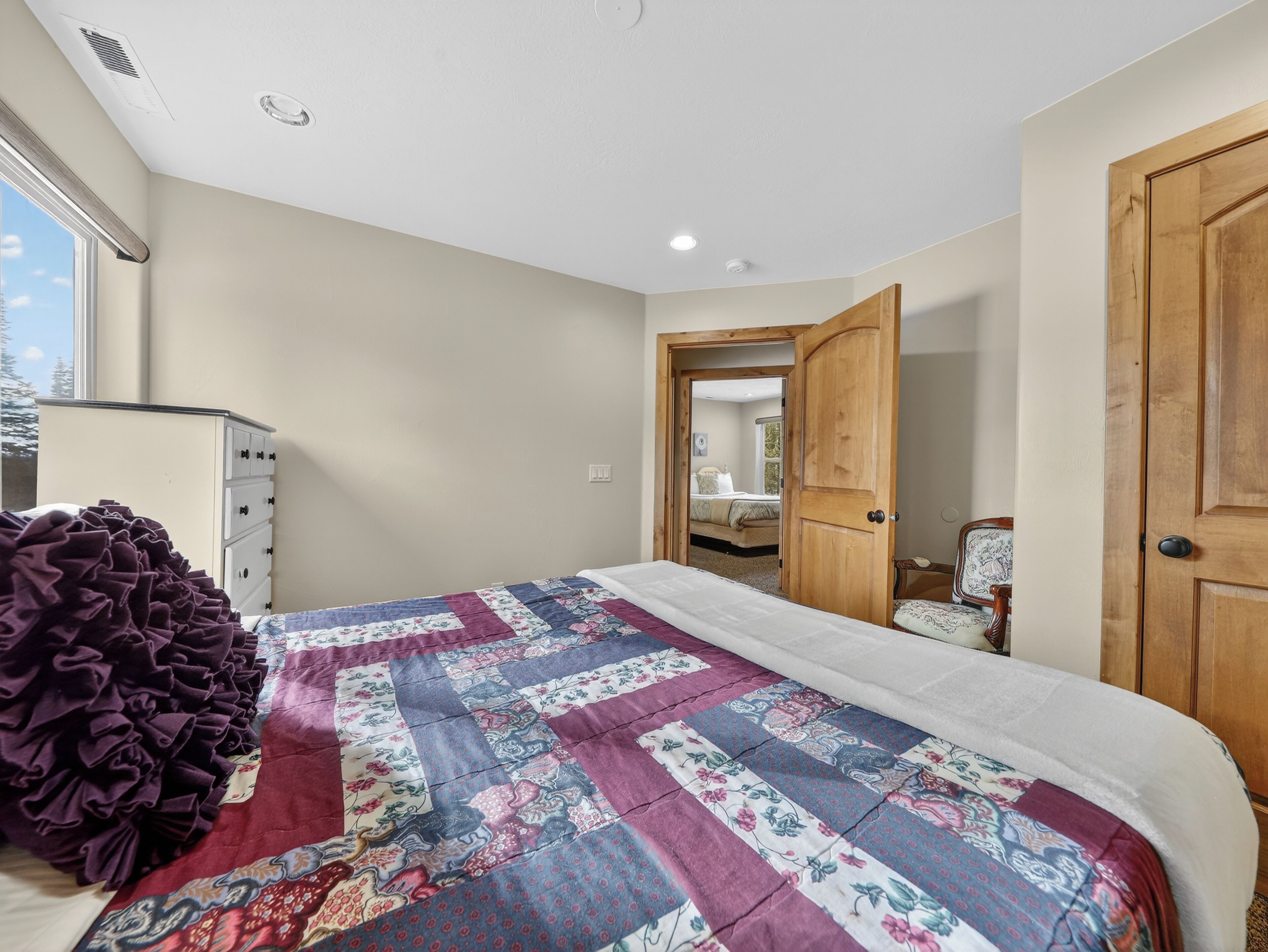 Une chambre à coucher avec un grand lit, une commode, une porte en bois et une fenêtre.