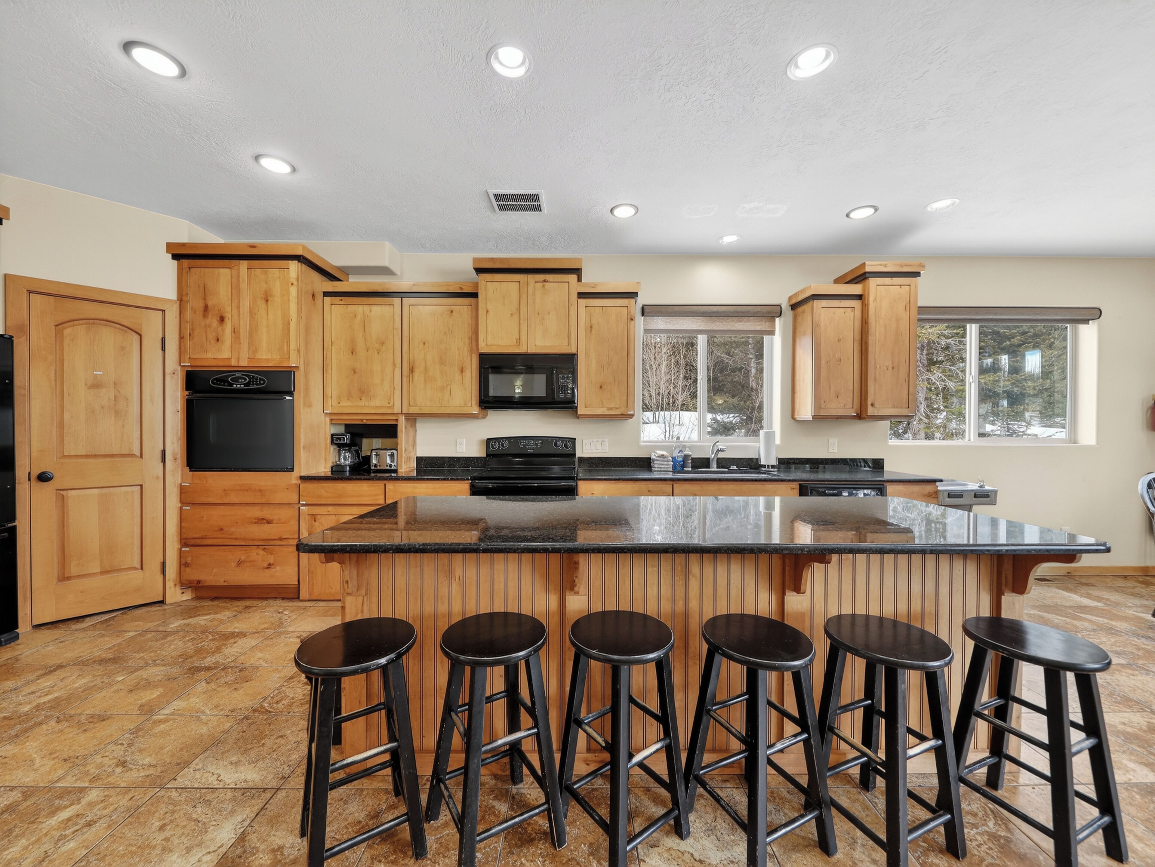 Una cocina amplia con armarios de madera, una isla grande con taburetes y un ventanal que proporciona luz natural.