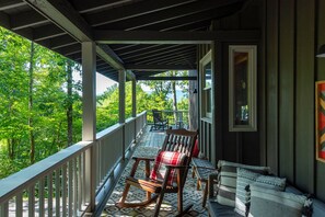 A covered porch with a view of a forest, a table with chairs, and a window.