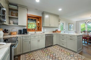 A modern kitchen with light-colored cabinets, a built-in dishwasher, and a patterned rug.