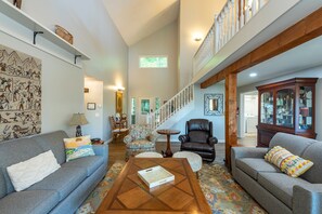 A spacious living room with a high ceiling, a staircase, and a view of the outdoors.