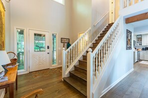 A spacious foyer with a wooden staircase, a dining area with a table and chairs, and a view of the outdoors through a glass door.