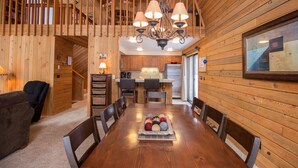 Un intérieur en bois comprenant une table à manger, des chaises, un lustre et un coin cuisine.