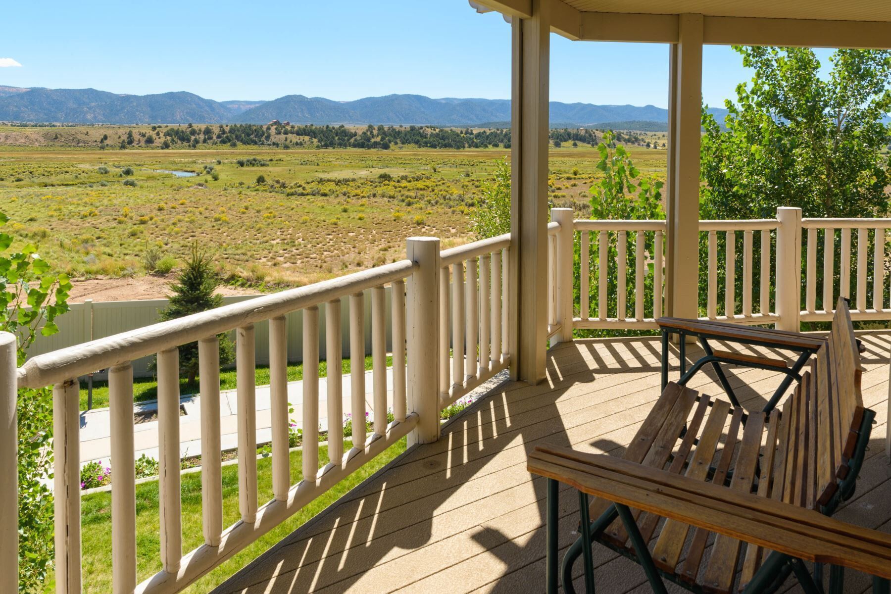 Une terrasse couverte avec un banc en bois et une vue sur une rivière et des montagnes.