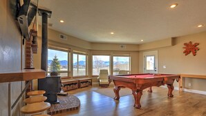 A spacious room with a pool table, a fireplace, and large windows offering a mountain view.