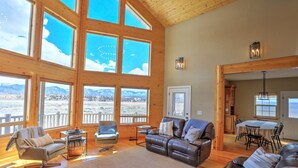 A spacious living room with large windows, a leather sofa, a dining table, and a view of mountains.