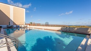 A swimming pool with clear blue water, a wooden deck, and a view of the beach.