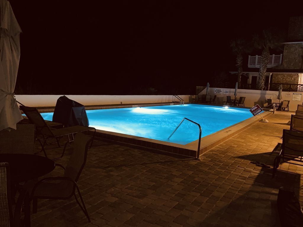 Une piscine nocturne à l’eau claire, entourée de chaises longues et dotée d’une terrasse carrelée.