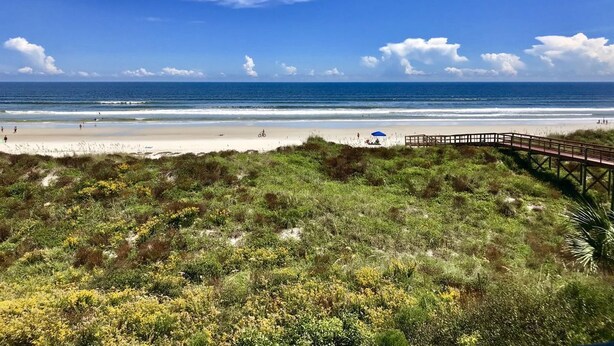 A beach with a wooden boardwalk, sandy shore, and grassy dunes.