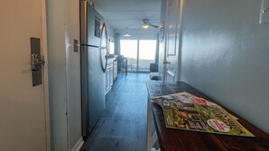 A narrow hallway with a wooden table, a refrigerator, and a ceiling fan.