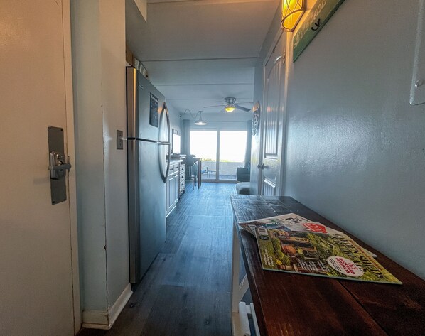 A narrow hallway with a wooden table, a refrigerator, and a ceiling fan.