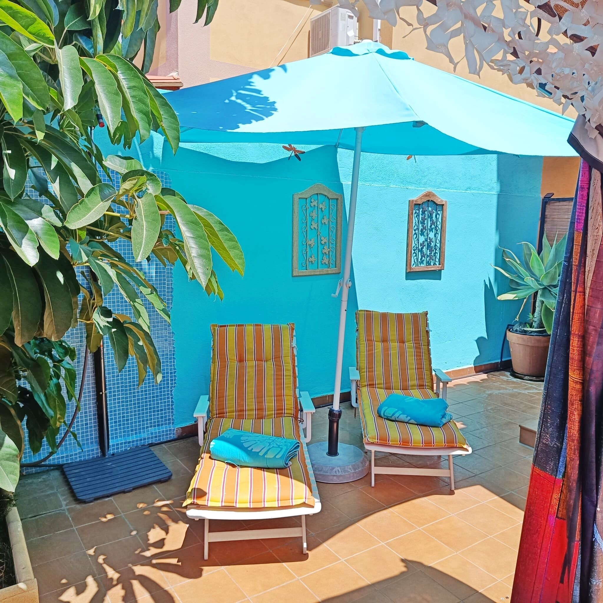 A sunlit outdoor seating area with two striped lounge chairs and a blue umbrella.