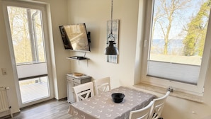 En matplats med ett bord för fyra personer, en tv som är monterad på väggen och en utsikt över träd genom fönstret.