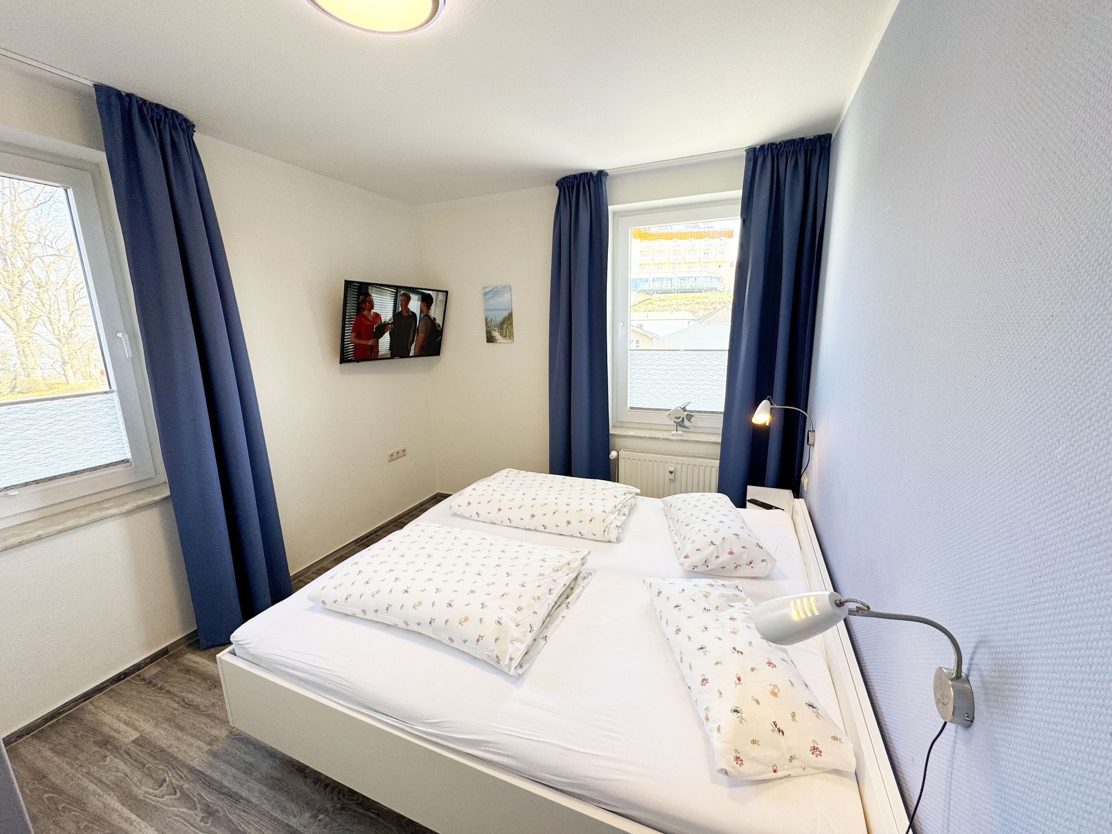 Ein Hotelzimmer mit Bett, Fernseher, Fenster mit Vorhängen und einer Lampe.