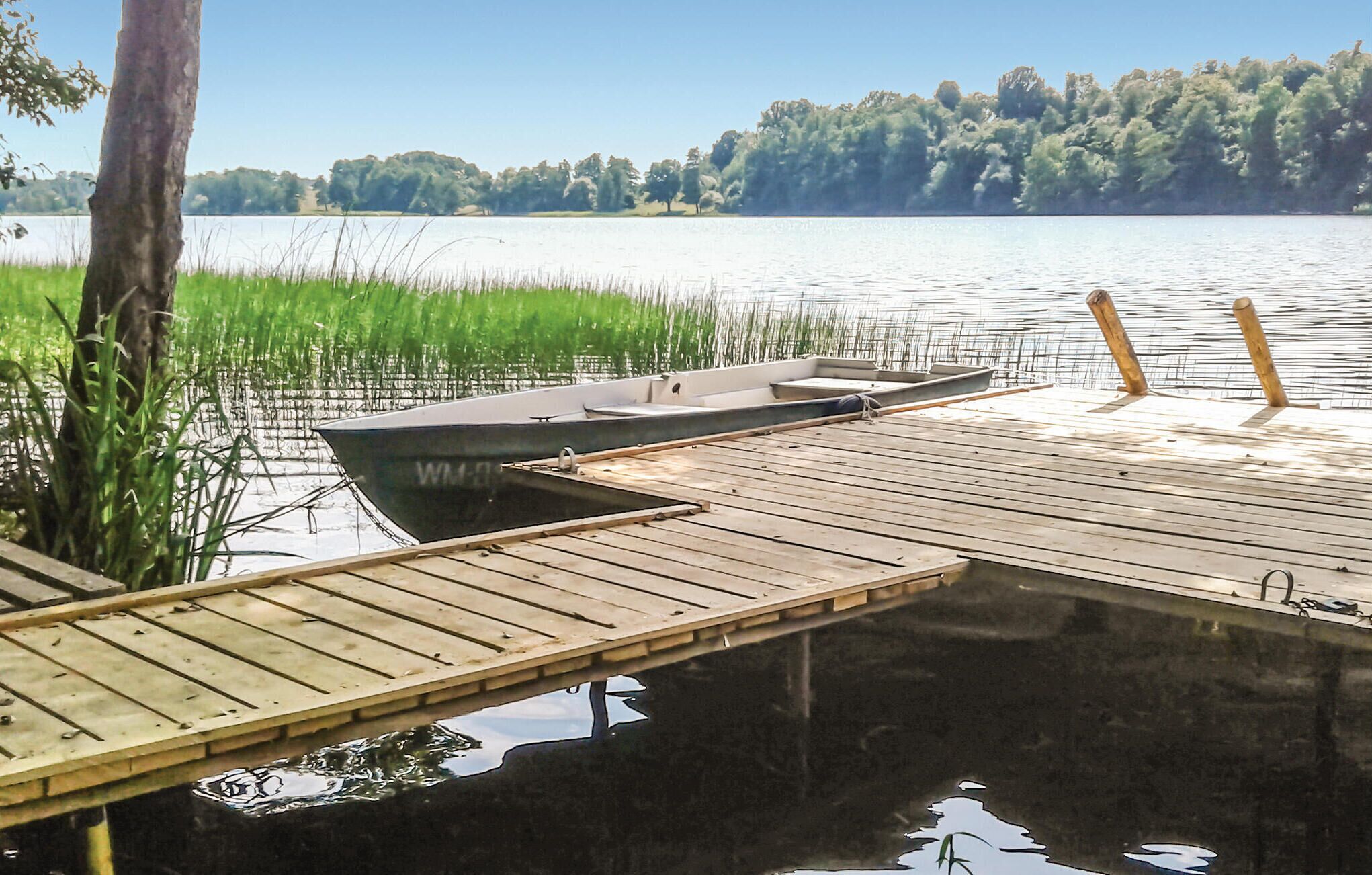 A wooden dock extending into a calm lake, surrounded by lush greenery and trees in the background.