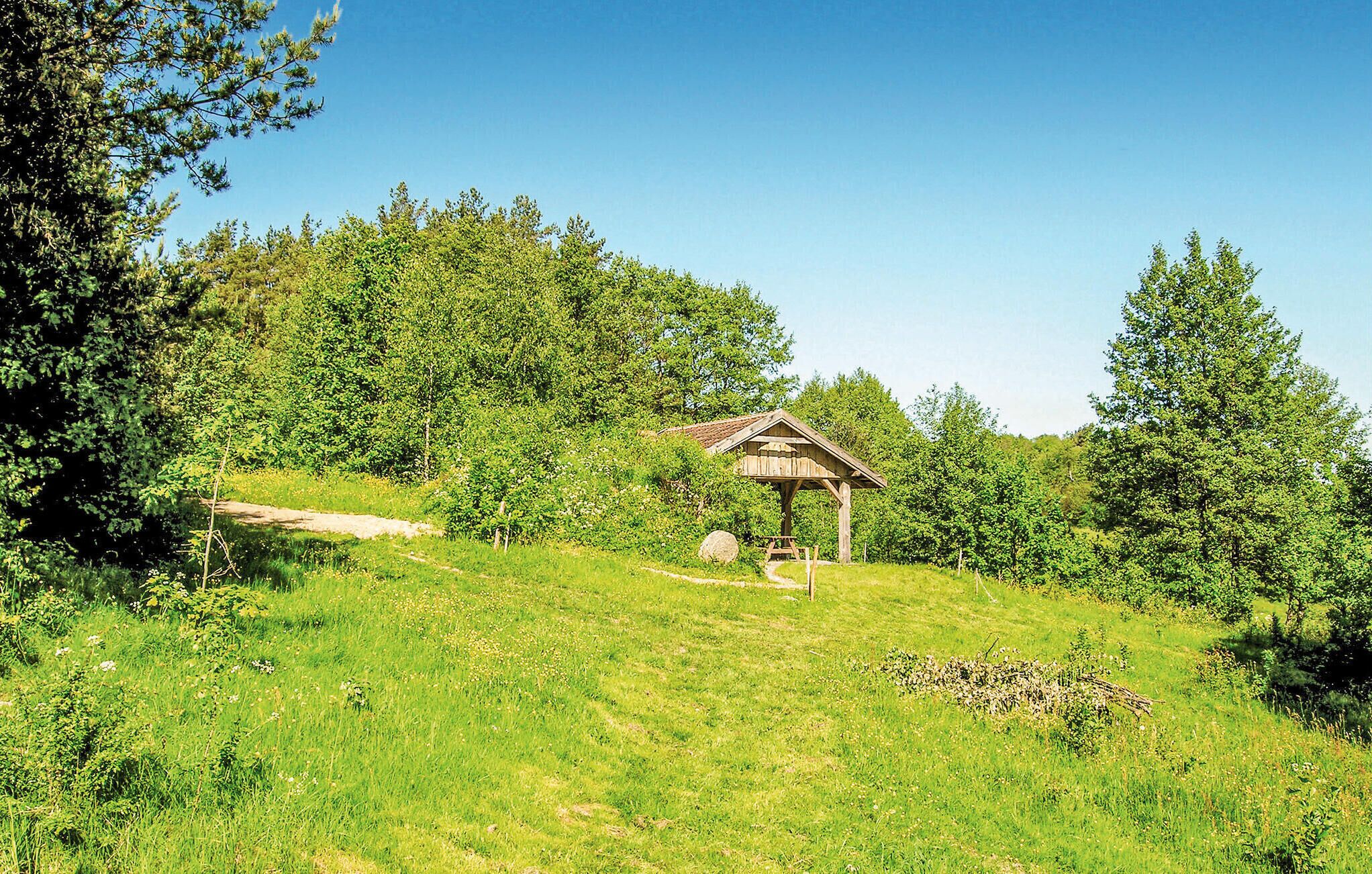 Un kiosque en bois se dresse dans un champ verdoyant, entouré d’arbres.