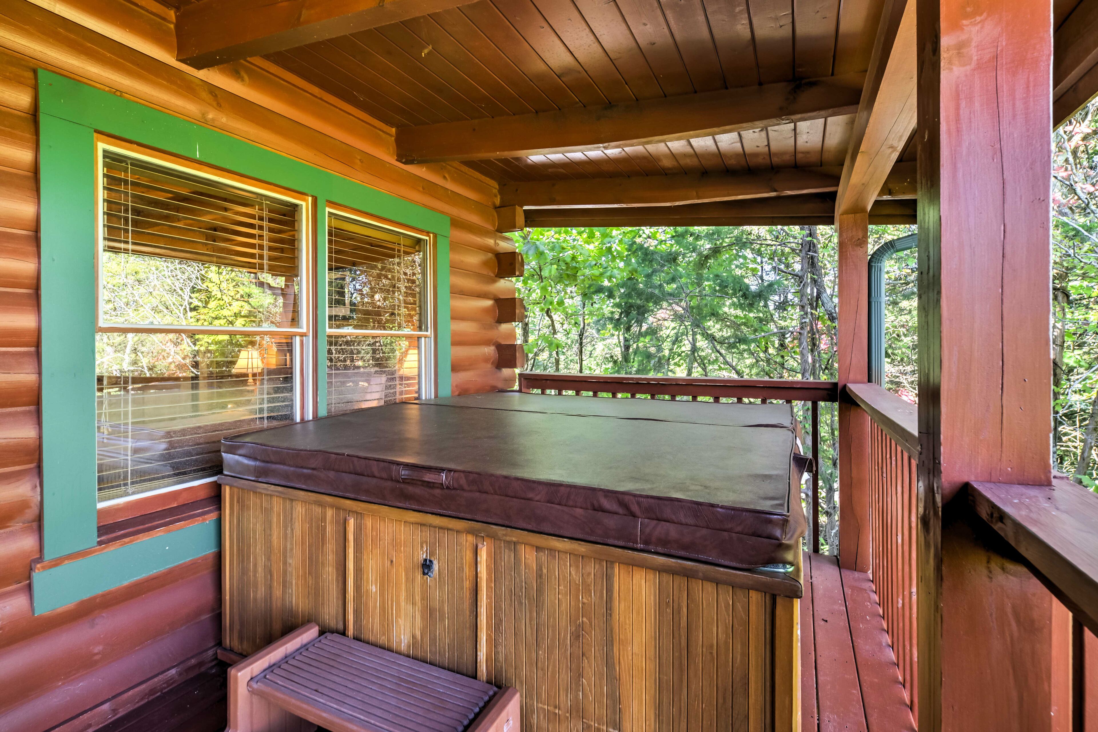 Una baita di legno con vasca idromassaggio, terrazza in legno e ampie finestre con vista sulla foresta.