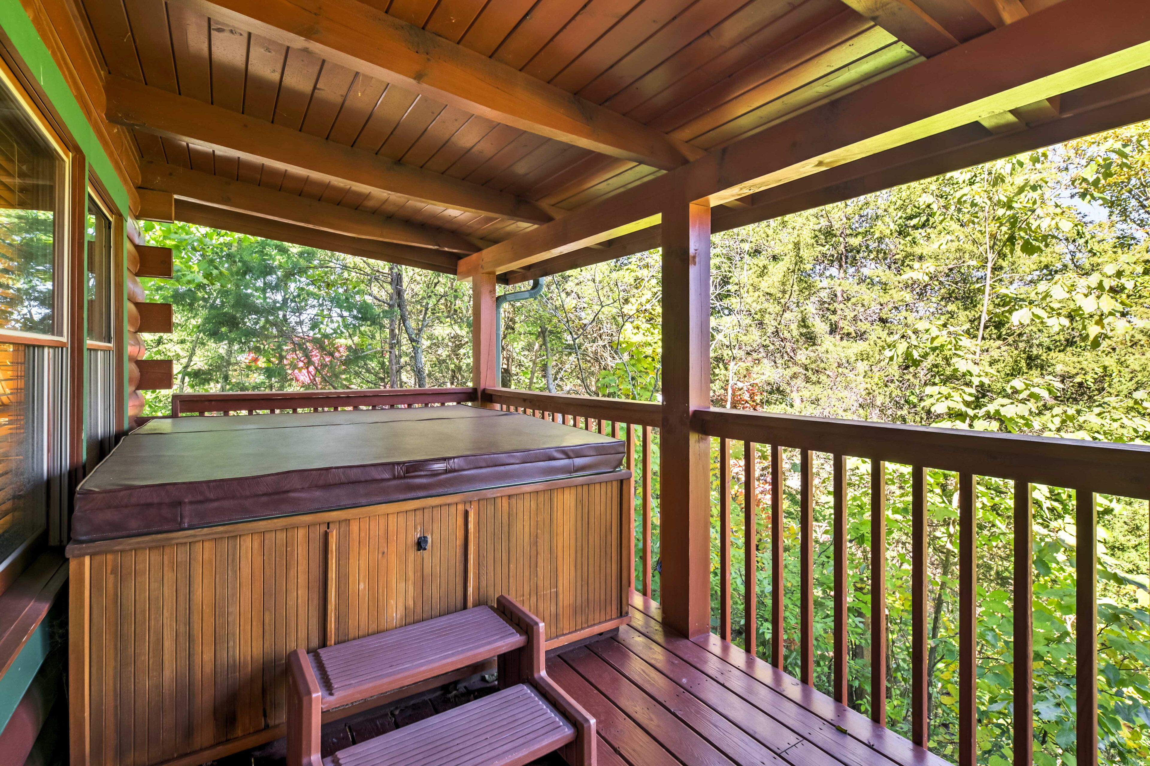Eine Holzterrasse mit Whirlpool und Sitzbereich, umgeben von üppigem Grün.