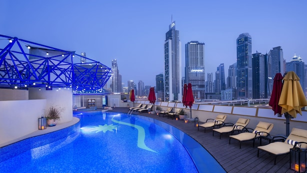 Piscina no terraço com espreguiçadeiras e guarda-sóis, com vista para o horizonte urbano e edifícios altos.