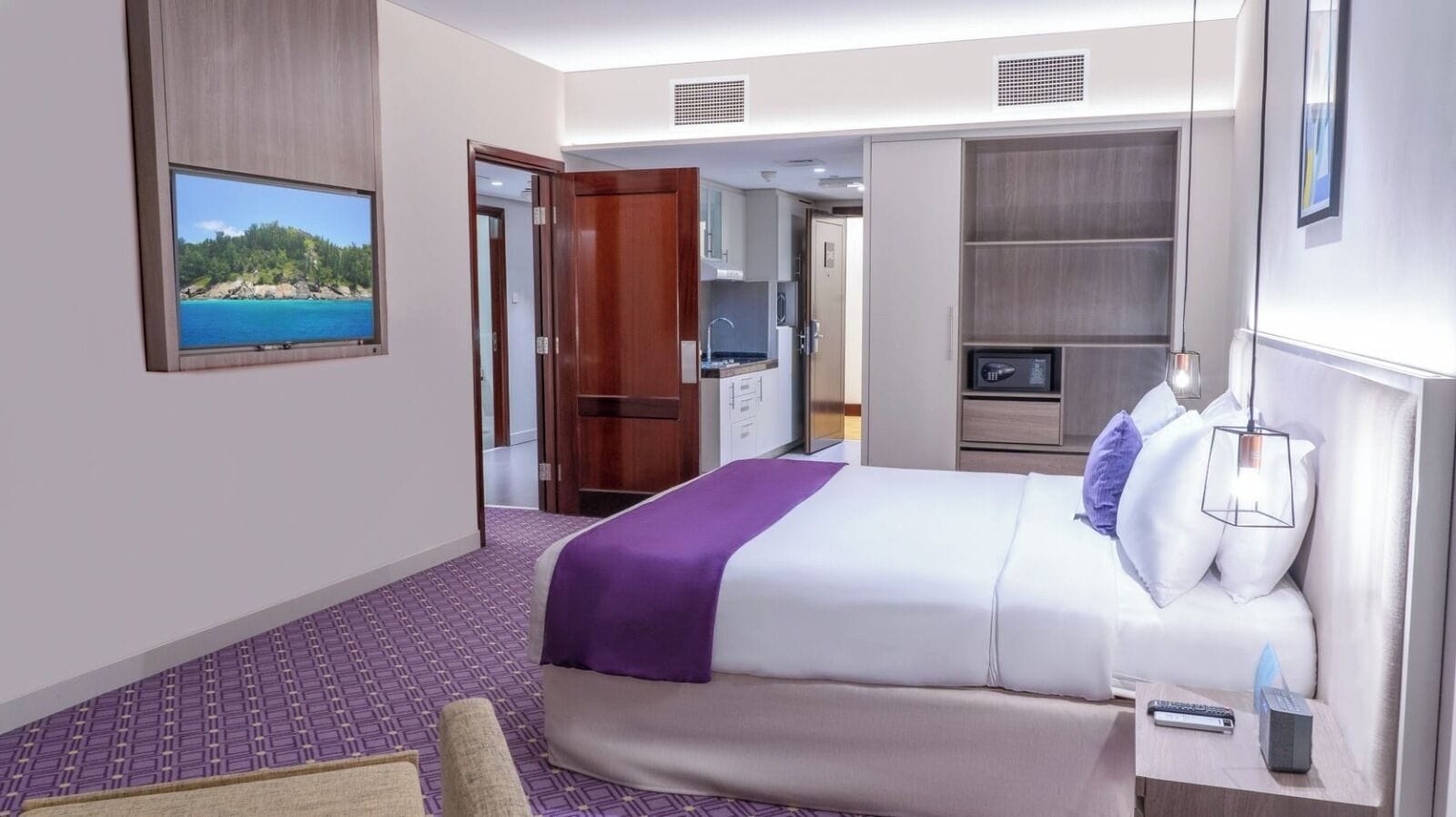 A hotel room with a bed, a desk, a chair, a TV, and a view of a beach.