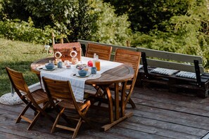 A round wooden table with a white tablecloth, surrounded by wooden chairs. A wicker basket and a bottle of juice are on the table.