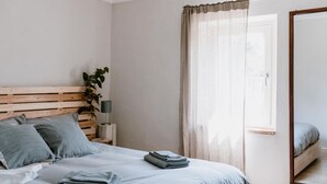 Ein ordentlich bezogenes Bett mit gefalteten Handtüchern, einem Holz-Kopfteil, einer Zimmerpflanze und einem Spiegel an der Wand.