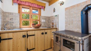 A kitchen with wooden cabinets, a sink, a window with a red checkered valance, a wall-mounted light fixture, and a stainless steel stove. - Pet friendly home in Perusic (Perusic)