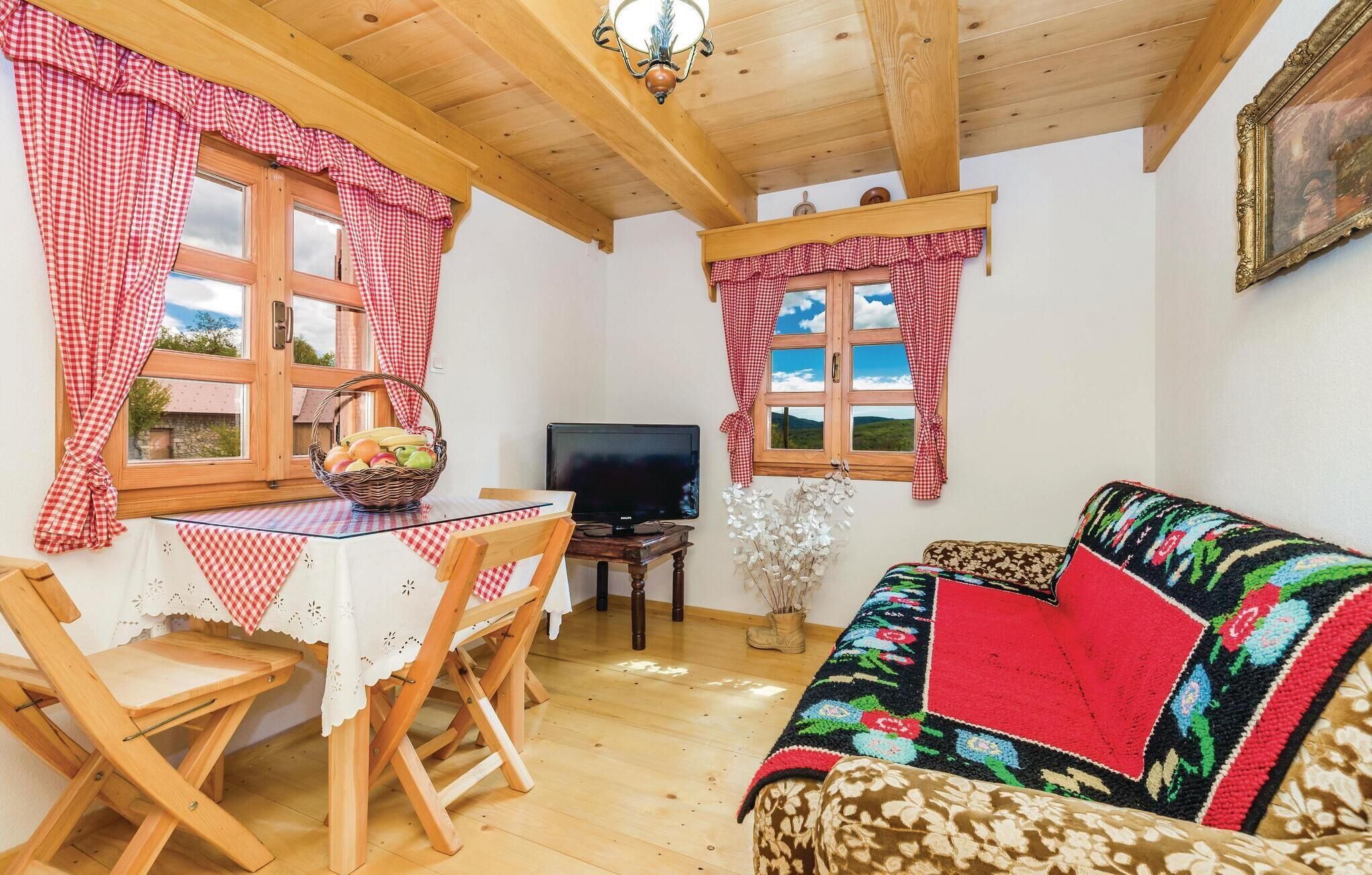Een gezellige kamer met houten plafond, een tafel met een mand vol fruit, een televisie, een bank en een raam met geruit gordijnen.