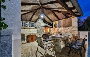 Enjoy dining al fresco in this charming outdoor space with a stone fireplace, wooden table, and pergola.
