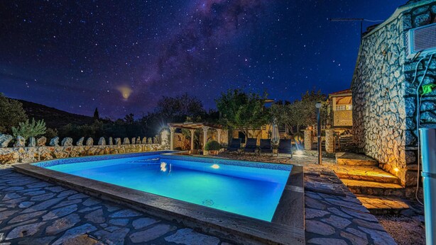 A swimming pool with stone tiles, surrounded by stone walls and a stone building with a balcony.