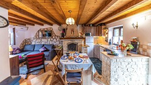 A cozy interior with a stone fireplace, wooden ceiling beams, a dining table set for four, and a kitchen area with a microwave and sink.