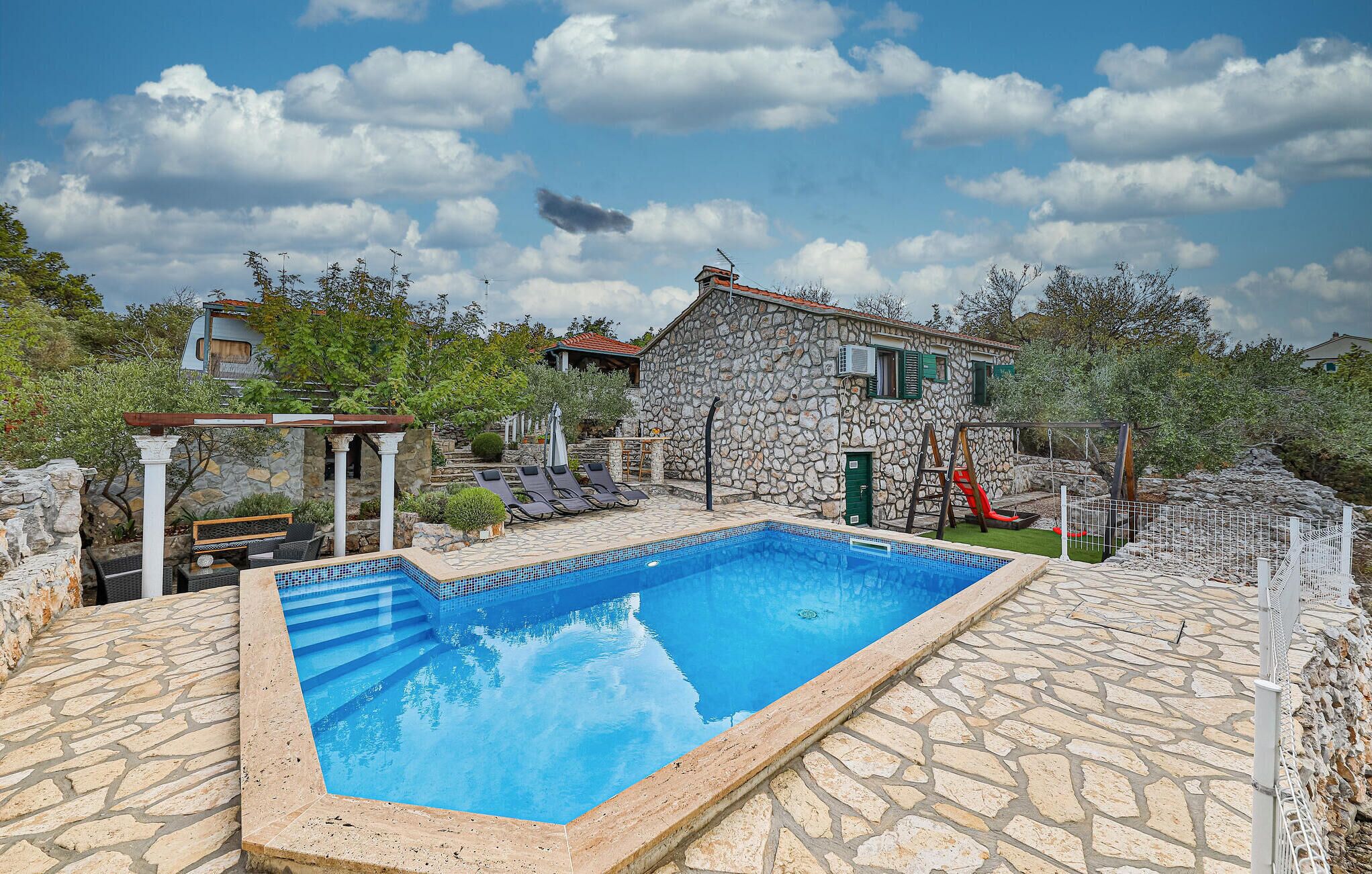 A stone building with a swimming pool, a pergola, and a children's play area.