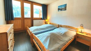 A bedroom with two wooden beds, a wooden dresser, a nightstand with a lamp, and a window with curtains. - Large apartment for 8 in Plagne Centre, balcony, pets allowed (La Plagne)