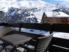 A balcony with wicker furniture overlooking a snowy mountain landscape and a wooden building. - Charming renovated 2-room apartment with south balcony, pets allowed (Méribel)