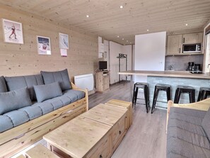 Un intérieur en bois comprenant un canapé, un banc, un coin cuisine et des tabourets de bar.