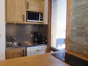 A kitchen with wooden cabinets, a stainless steel sink, a Bosch dishwasher, and a window with blinds. - Charming renovated 2-room apartment with south balcony, pets allowed (Méribel)