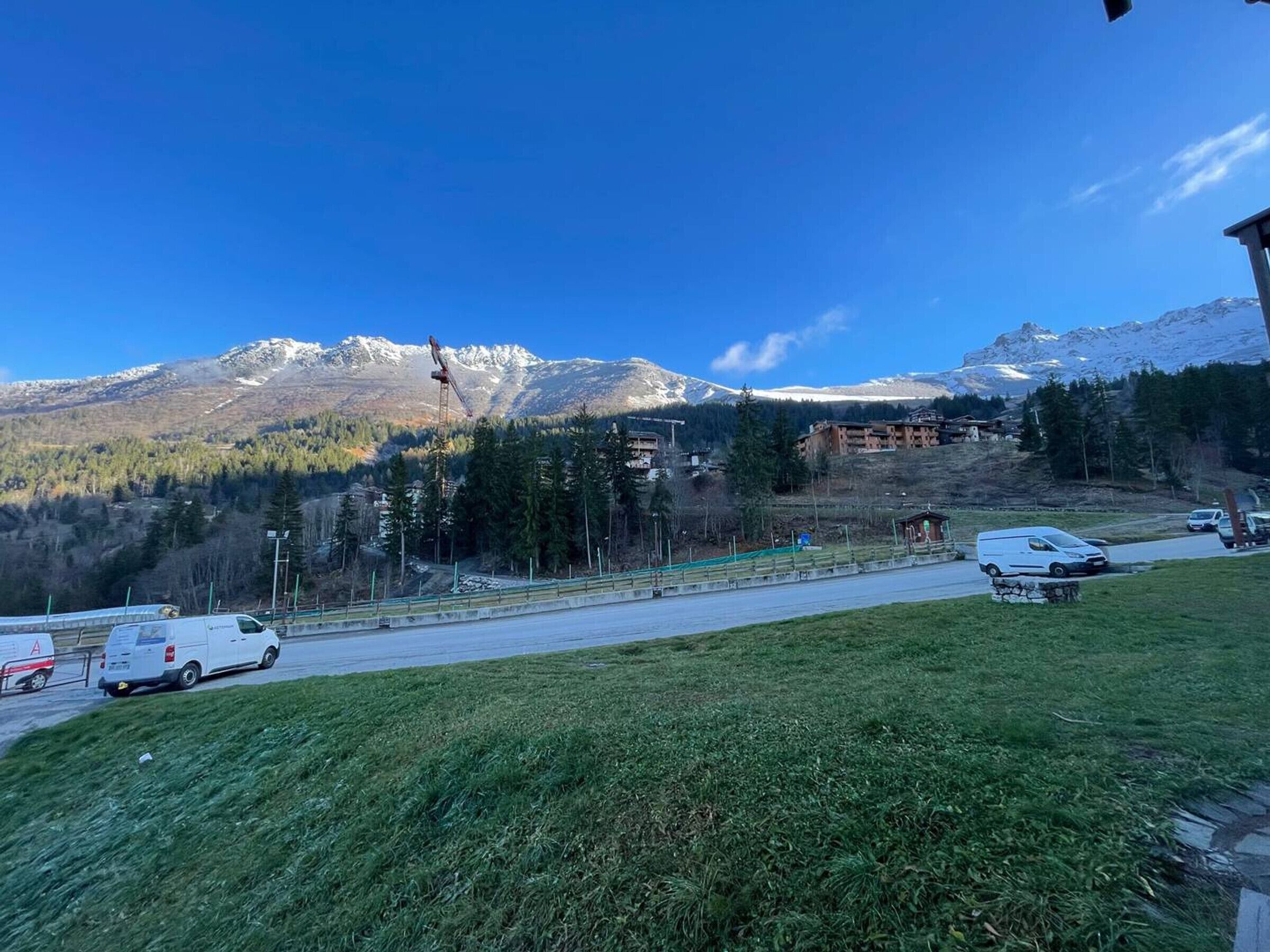 Una carretera con vehículos, una zona verde y un paisaje montañoso con edificios al fondo.