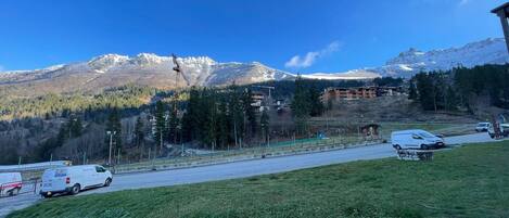 Una carretera con vehículos, una zona verde y un paisaje montañoso con edificios al fondo.