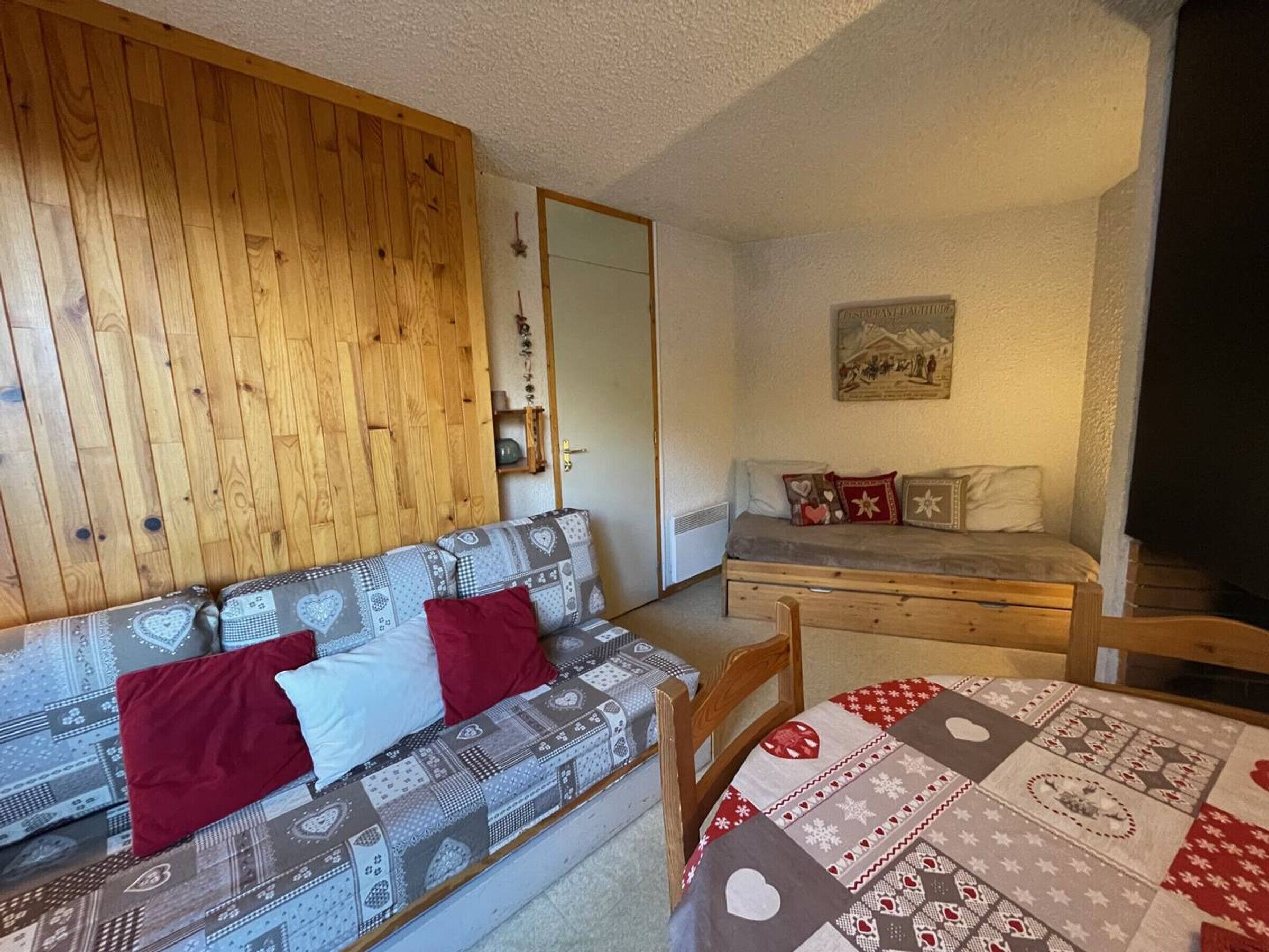 A cozy room with a wooden wall, a patterned sofa, a small bed, and a table with a quilt.