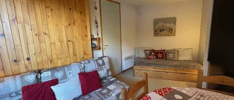 Una habitación acogedora con una pared de madera, un sofá estampado, una cama pequeña y una mesa con colcha.