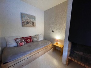 A cozy room with a bed, a small table, a wall-mounted picture, and a fireplace. - 1-bedroom in central Valmorel, close to shops and lifts (Valmorel)