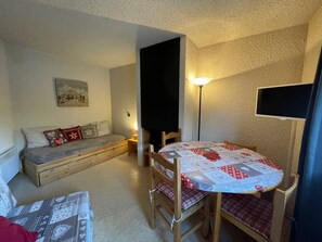 A cozy room with a sofa, a table with chairs, a flat-screen TV, and a lamp.