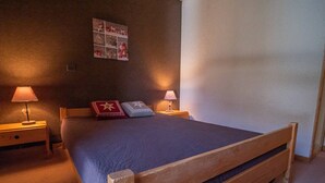 A bedroom with a wooden bed, two bedside lamps, a nightstand, a wall-mounted picture, and a carpeted floor.