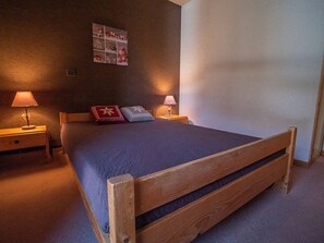 A bedroom with a wooden bed, two bedside lamps, a nightstand, a wall-mounted picture, and a carpeted floor. - 1-bedroom in central Valmorel, close to shops and lifts (Valmorel)